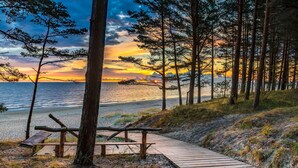 A wooden pathway leading to a bench by the beach, surrounded by tall trees and a sunset view. - Rixwell Collection Seaside Hotel Jurmala (Jurmala)