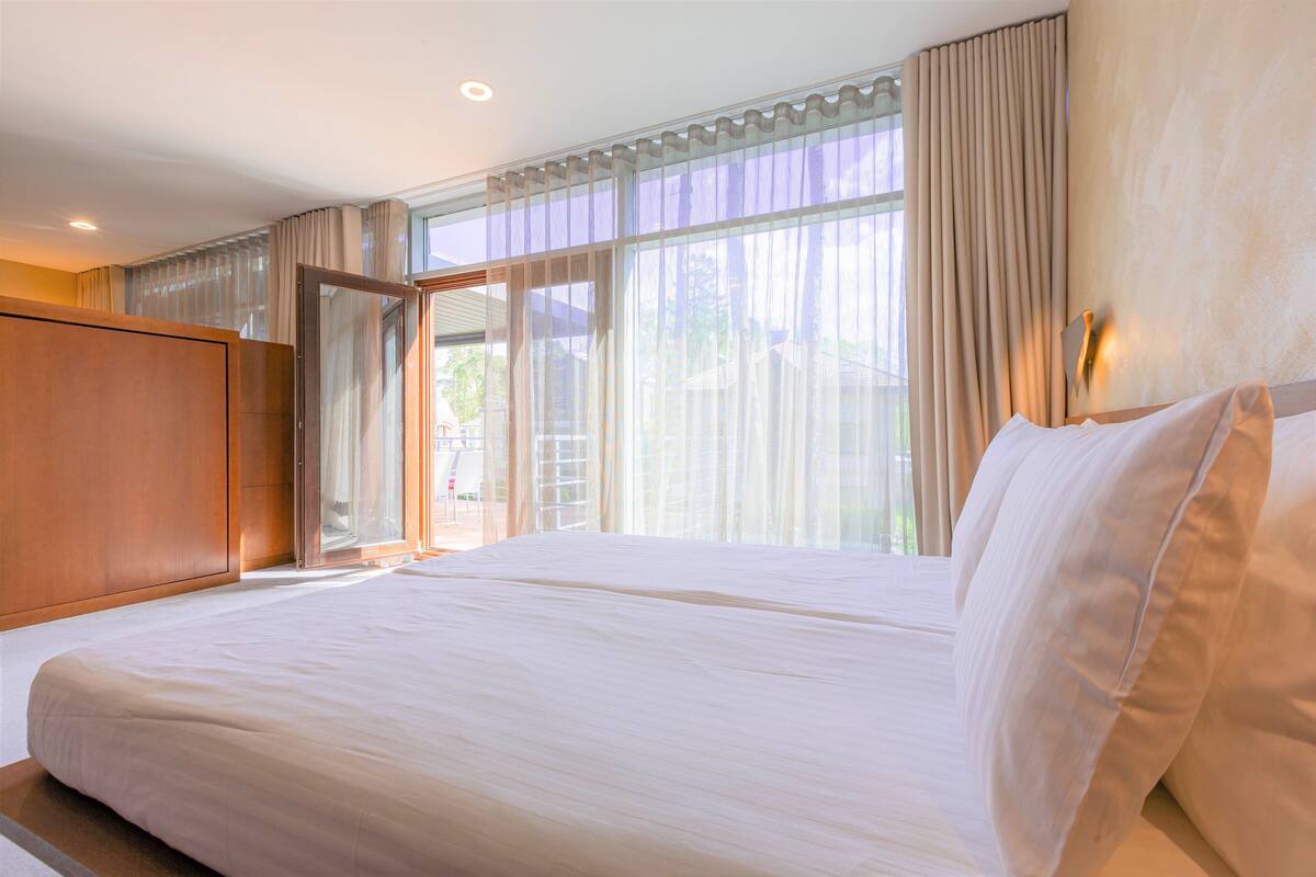 A hotel room with a large bed, a wardrobe, and a sliding glass door leading to a balcony.