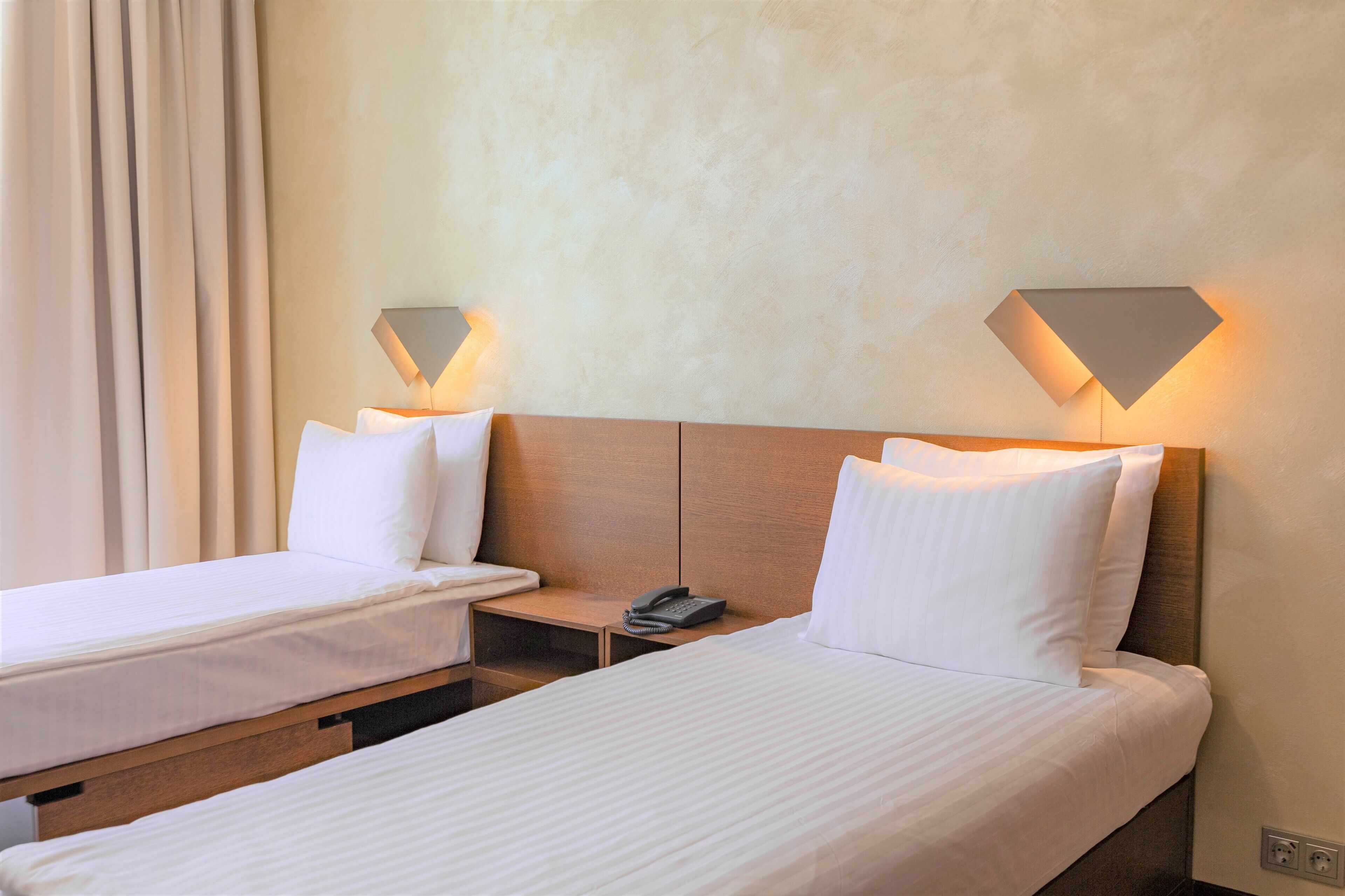 Une chambre d’hôtel avec deux lits simples, une tête de lit en bois, des tables de chevet avec des lampes et un téléphone.