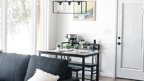 En moderne stue med en mørkegrå sofa, et sofabord og et spiseområde med bord og stole. Der er et træloft og en hvid dør i baggrunden.