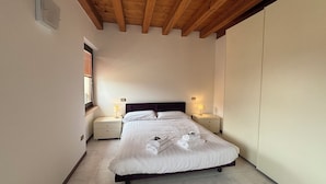 A bedroom with a wooden ceiling, a bed with white linens, two bedside tables with lamps, and a window with blinds. - VERONETTA 52 (Verona)