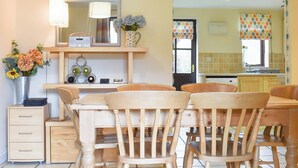 A dining area with a wooden table and chairs, a radio, a vase with flowers, and a kitchen in the background. - 3 bedroom accommodation in Whitby (Whitby)