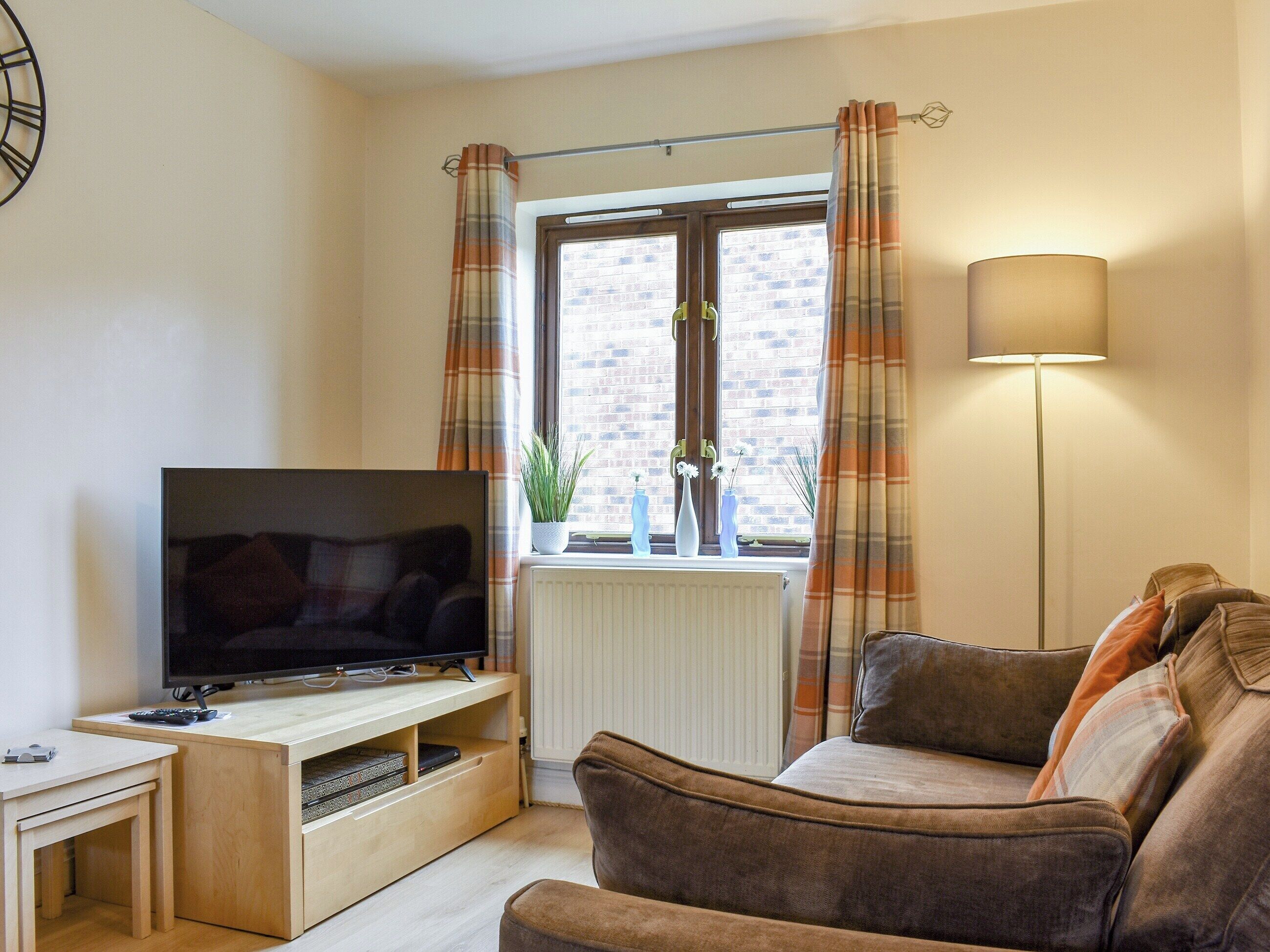 A living room with a TV on a wooden stand, a sofa, a floor lamp, and a window with curtains.