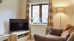 A living room with a TV on a wooden stand, a sofa, a floor lamp, and a window with curtains. - 3 bedroom accommodation in Whitby (Whitby)