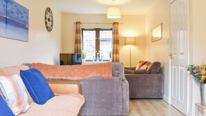 A living room with a sofa, two armchairs, a television, and a door. - 3 bedroom accommodation in Whitby (Whitby)