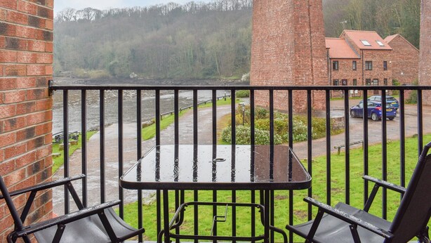 A balcony with a table and chairs, overlooking a river and a brick building. - 3 bedroom accommodation in Whitby (Whitby)