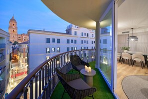 Ein Balkon mit Korbmöbeln, einem Tisch mit Kerzen und Blick auf ein historisches Gebäude.