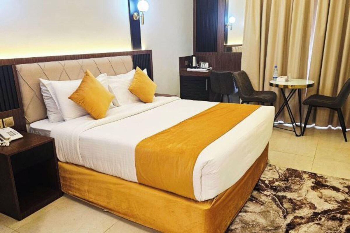 Una habitación de hotel con una cama grande, un escritorio, dos sillas, una mesita y un teléfono en la mesita de noche.