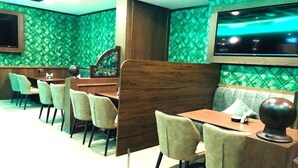 En restaurang med grönt mönstrade väggar, trämöbler och en tv som är monterad på väggen.