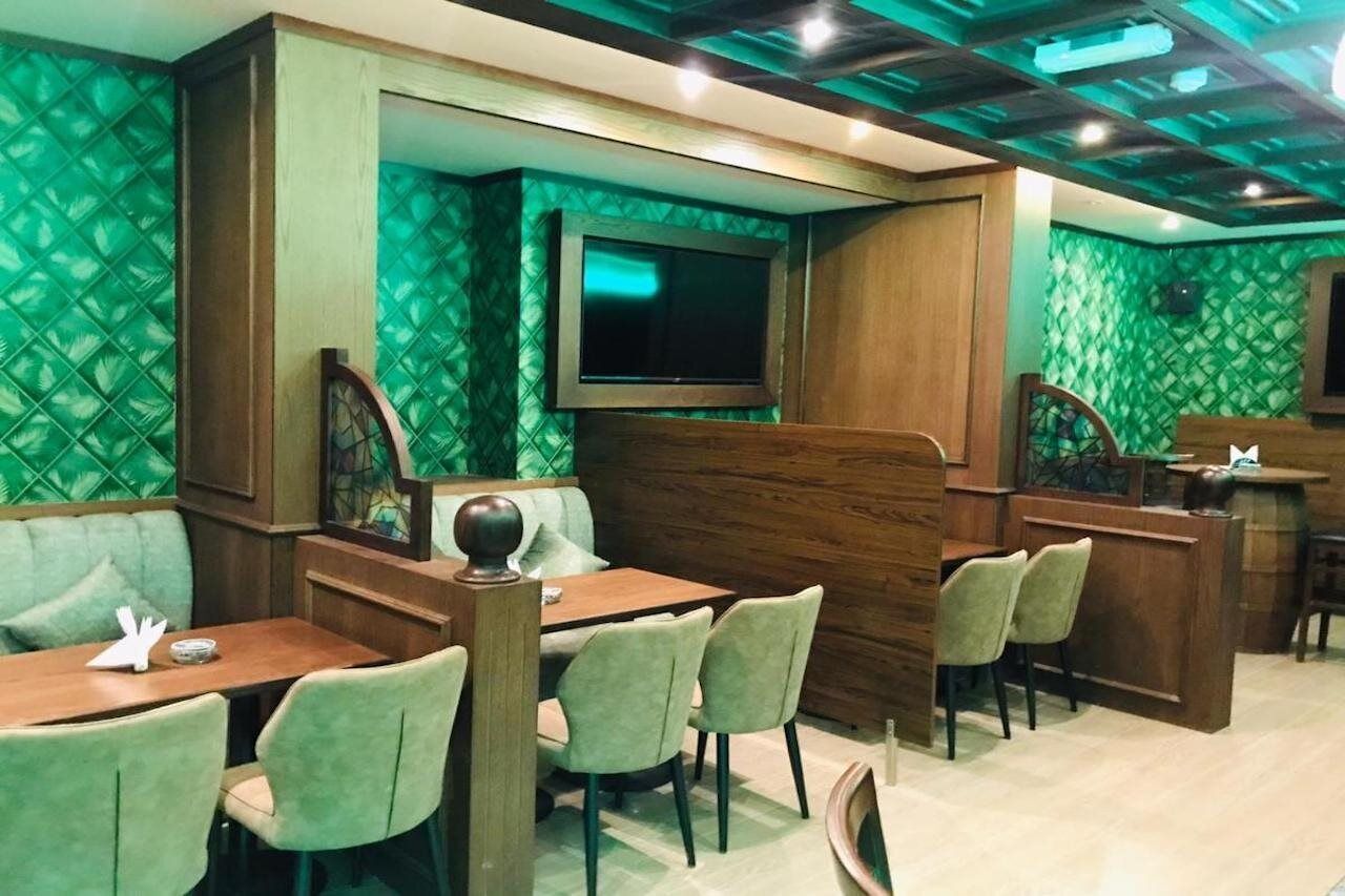 Un restaurante con cabinas y mesas, paredes de diseño verde y un televisor montado en la pared.