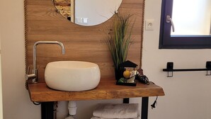 Een badkamer met een houten wastafelmeubel, een ronde spiegel, een witte wastafel en een handdoekhouder.