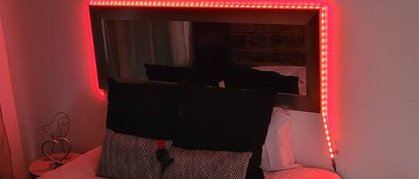 A bed with a mirror and LED lights, a heart-shaped decoration above the mirror, and rose petals on the bed.