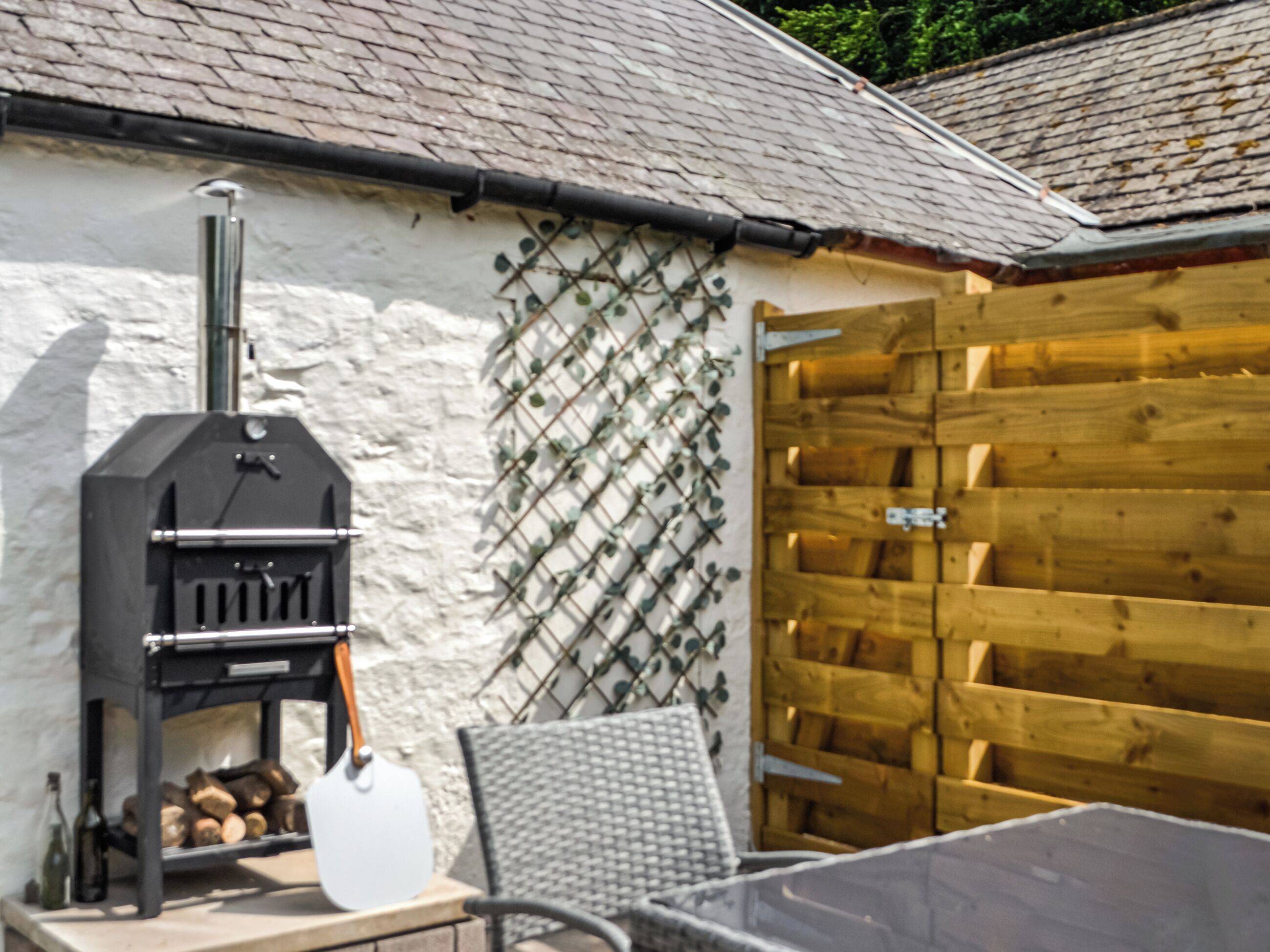 Un barbecue, une clôture en bois et une table avec des chaises.