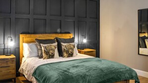 A bedroom with a wooden headboard, two bedside tables, a green blanket, and a wall panel design. - Terraughtie Cottage West-UK43408 (Dumfries)