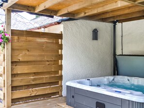 A wooden deck with a hot tub and a white wall.