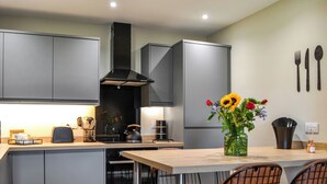 A modern kitchen with grey cabinets, a black range hood, a wooden island with bar stools, and a vase with flowers. - Terraughtie Cottage West-UK43408 (Dumfries)