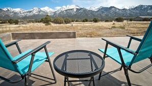 Two turquoise chairs and a round table on an outdoor patio with a mountain view. - Whispering Hills Retreat (Saguache County)