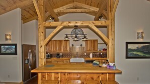 A rustic kitchen with wooden beams, a large island with bar stools, and a hanging light fixture. - Whispering Hills Retreat (Saguache County)
