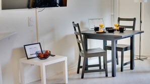 Een eetgedeelte met een ontbijttafel, inclusief croissants en sinaasappelsap. Er staat een klein wit tafeltje met een fruitmand en een ingelijst certificaat.