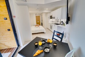 Quarto de hotel moderno com área de refeições, cozinha compacta e uma cama.