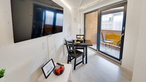 Een modern appartement met een eethoek, een aan de muur bevestigde televisie en een balkon met zitplaatsen.