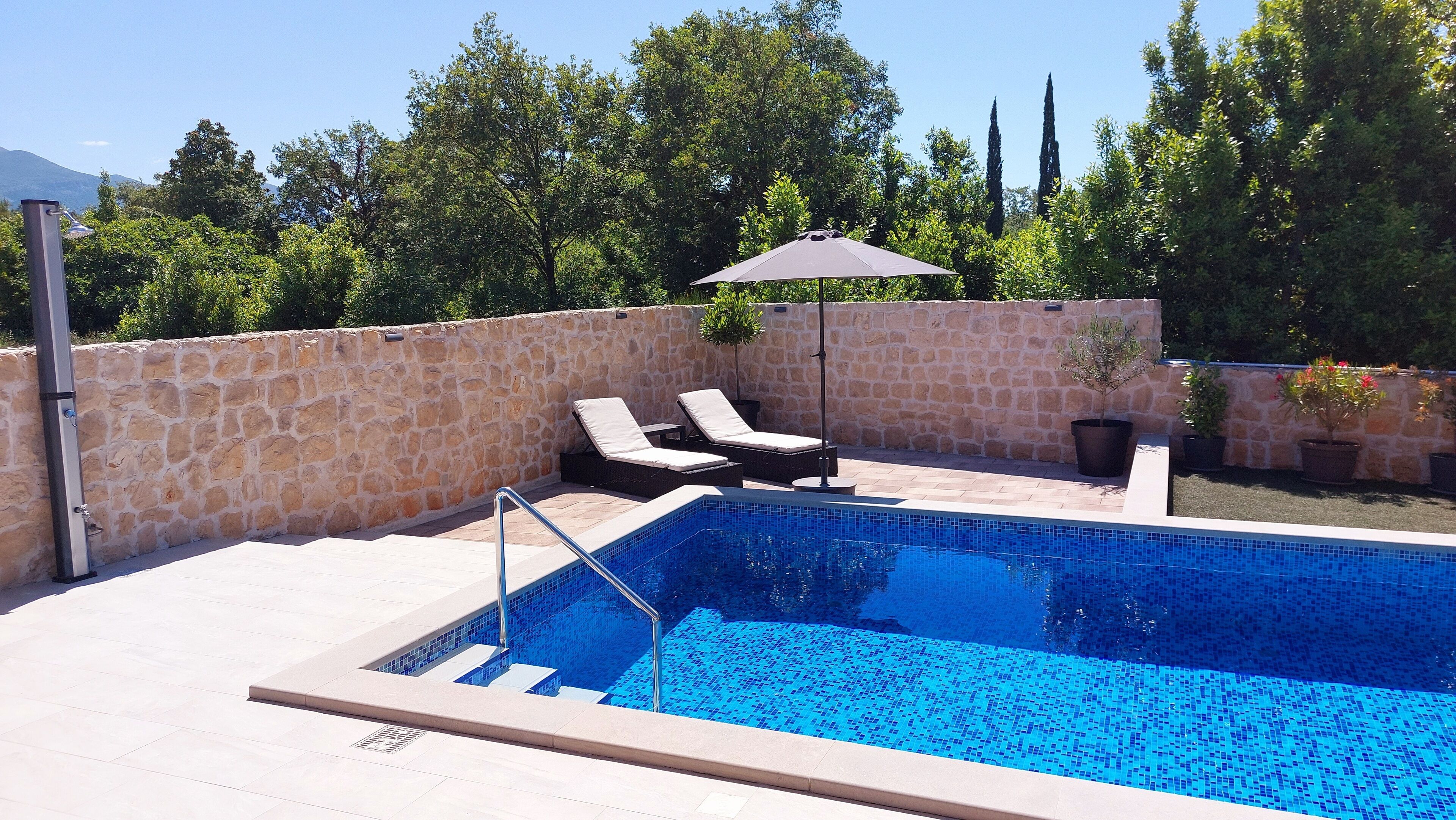 Une piscine avec deux chaises longues et une petite table, entourée de murs en pierre et de plantes en pot.