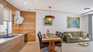 A modern kitchen with a built-in oven, a dining area with a wooden table and chairs, a green sofa, and a painting on the wall.