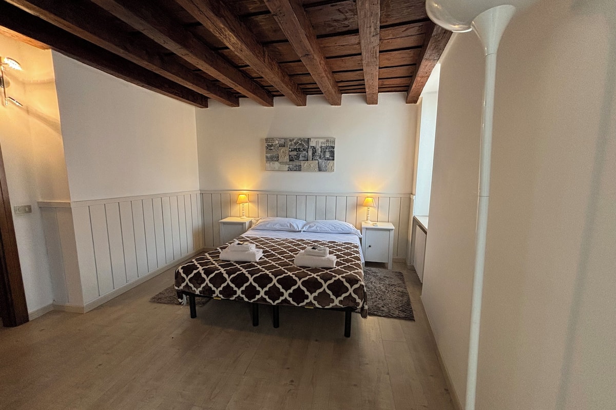 A bedroom with a bed, two bedside tables, a headboard, a wooden ceiling, and a wall-mounted picture.