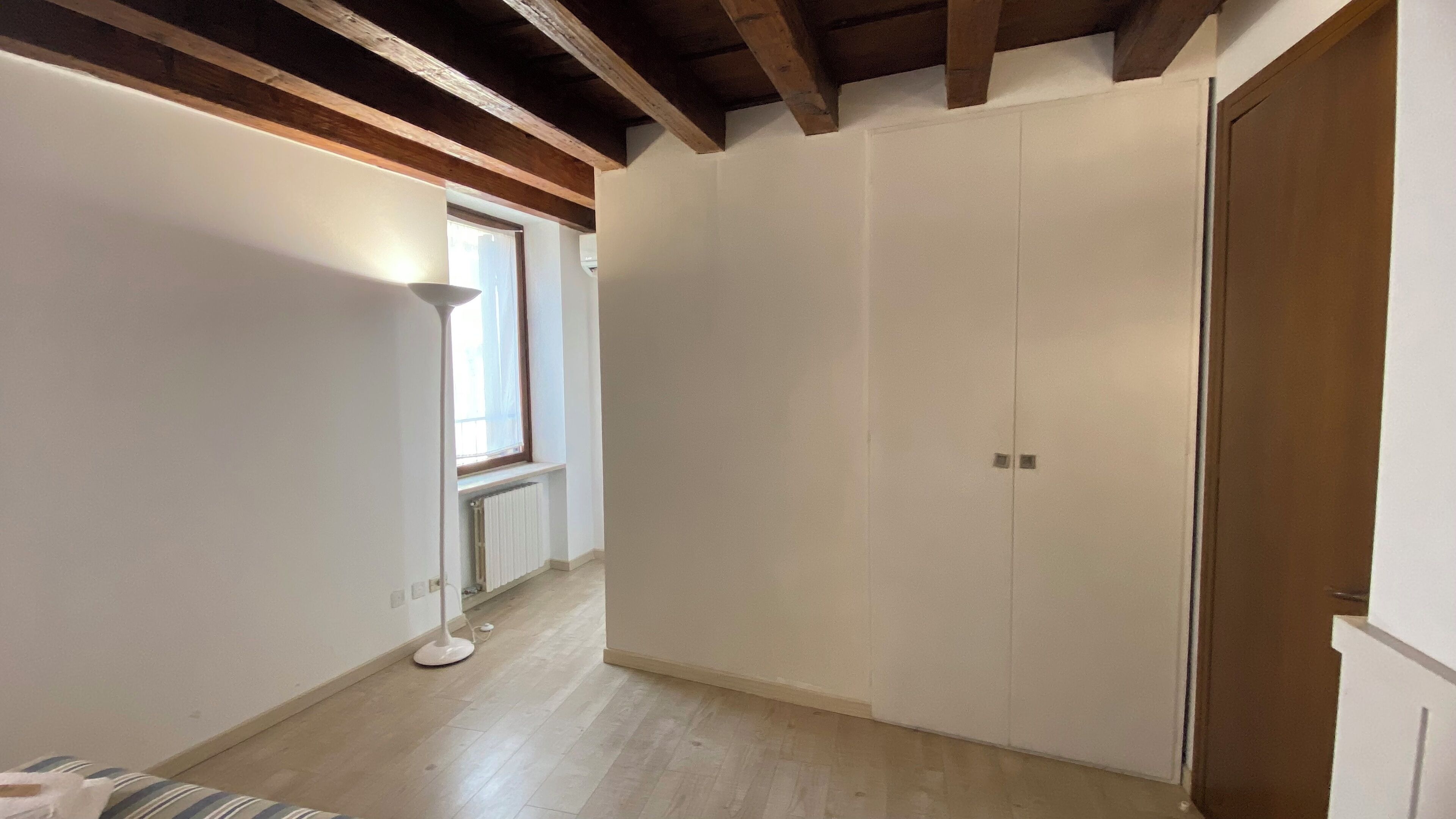 Ein schmaler Korridor mit Holzbalken an der Decke, einem Heizkörper und einem Fenster.