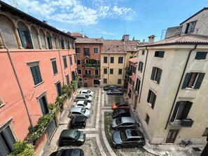 A narrow street lined with parked cars and buildings with balconies and arched windows. - CORTEBELLA (Verona)