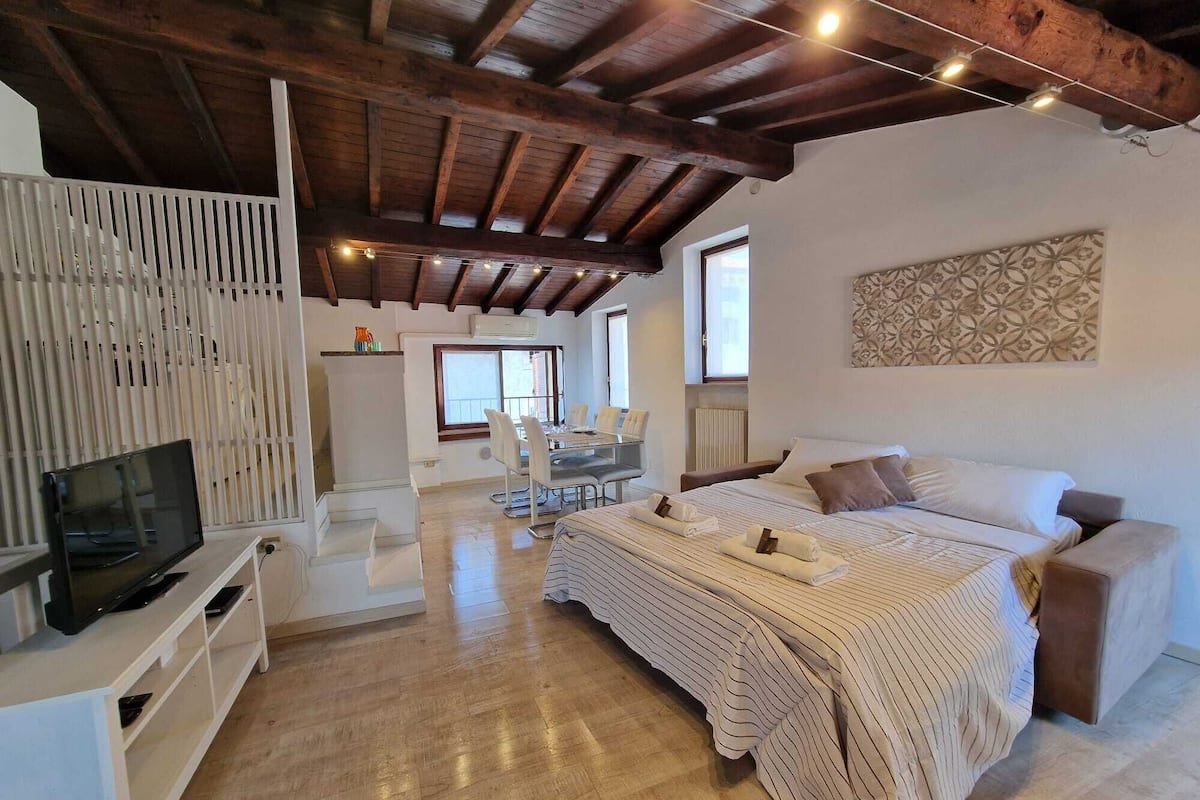 A spacious room with a bed, a TV, a dining area, and a staircase.