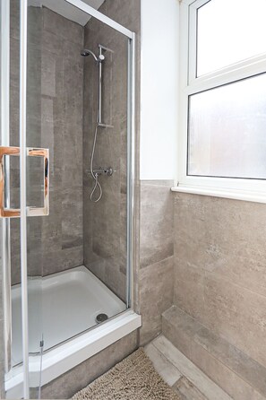 Eine begehbare Dusche mit Glastür, eine Badewanne und ein Fenster.