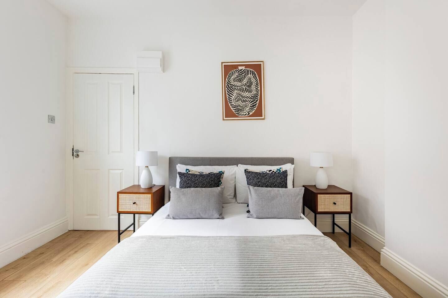 A bedroom with a bed, two nightstands, a door, and a wall-mounted artwork.