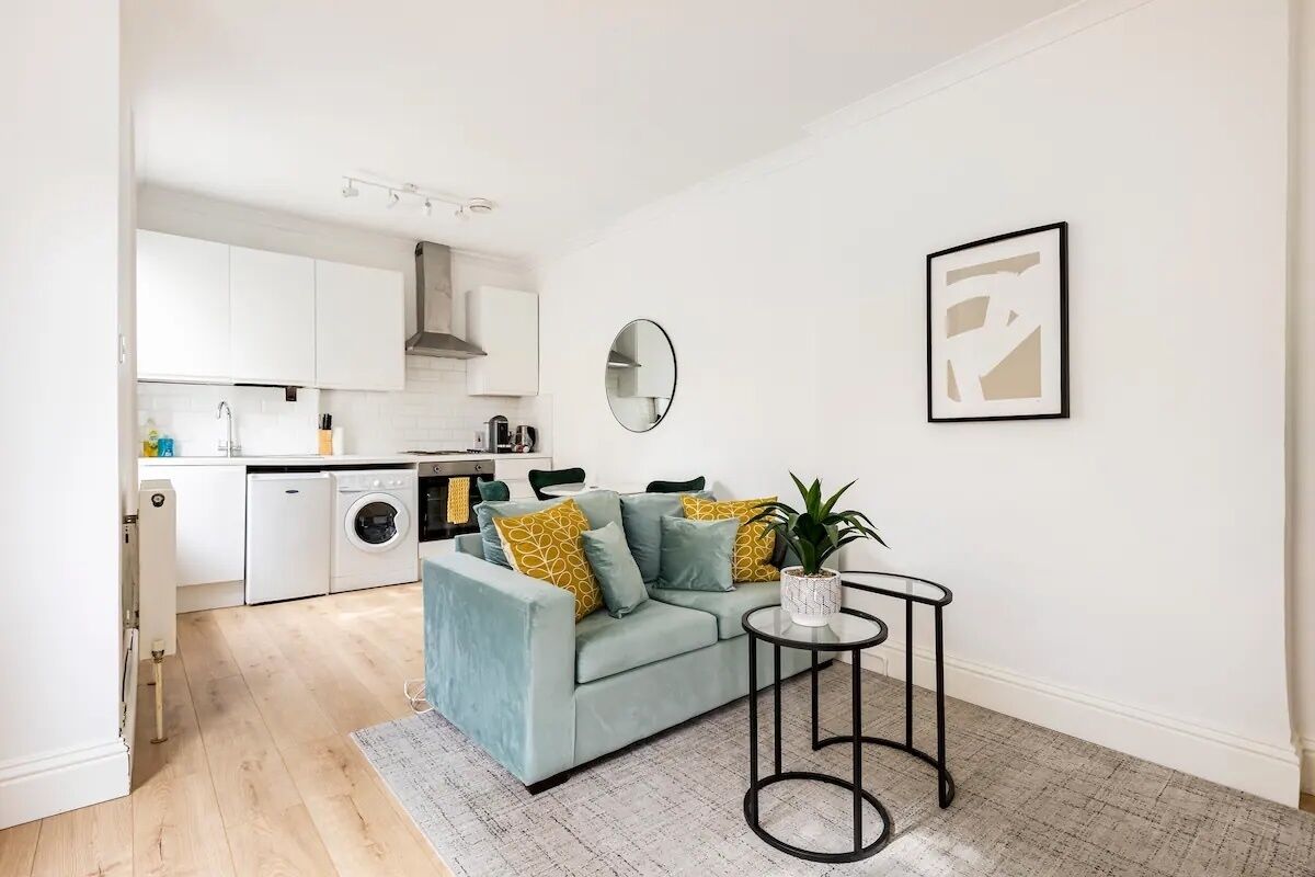A modern living room with a light blue sofa, a round mirror, and a small table with a plant.