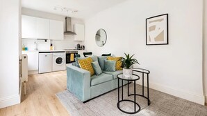 A modern living room with a light blue sofa, a round mirror, and a small table with a plant. - Stylish one bedroom apartment in Greater London (London)