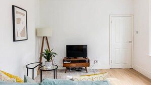 A living room with a television, a lamp, a plant, and a door. - Stylish one bedroom apartment in Greater London (London)