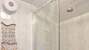 Un baño con cabina de ducha de vidrio, tocador blanco y un adorno en la pared.