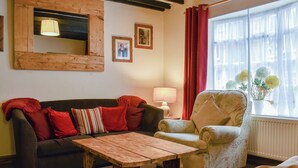 Una sala acogedora con una mesa de centro de madera, un sofá con cojines rojos, un sillón estampado y una ventana con cortinas.