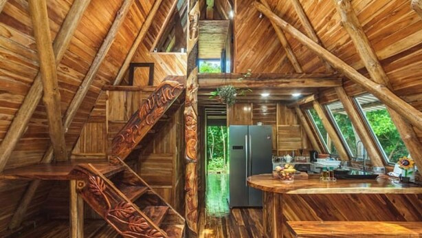 Een houten hutje met een keukenhoek, een trap en een klein balkon.