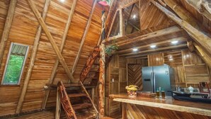 Een rustiek houten interieur met een wenteltrap, een keuken met een koelkast en een raam met uitzicht op groen.