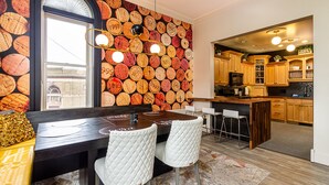 Un coin repas agrémenté d’un mur décoré d’objets circulaires, d’une table à manger en bois, de chaises blanches et d’une cuisine en arrière-plan.