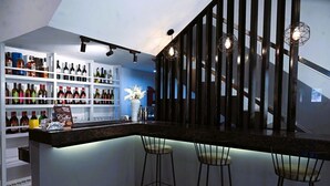 Un área de bar moderna con una barra oscura, estantes blancos con varias botellas y tres taburetes de bar.