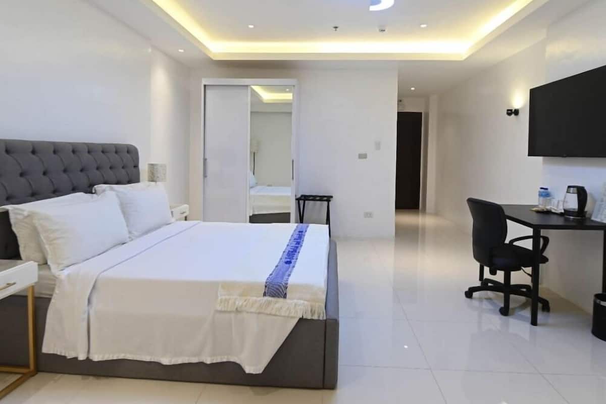 A modern hotel room with a large bed, a desk, and a flat-screen TV.