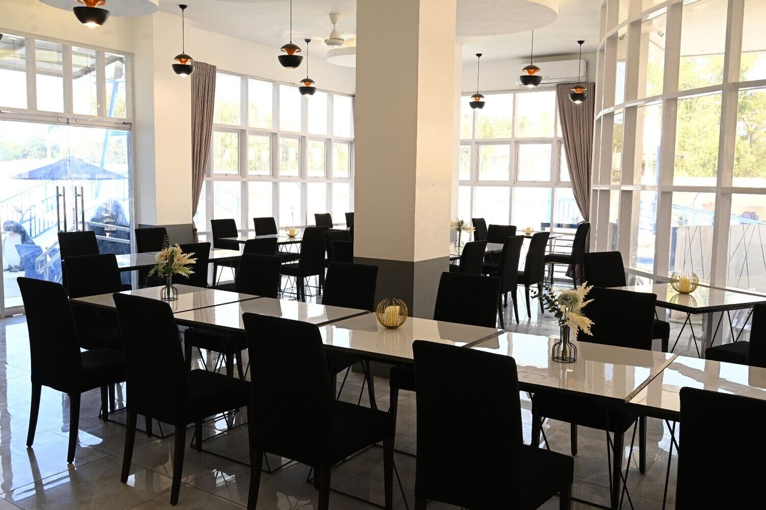 Un vaste espace dédié à la salle à manger, avec de nombreuses tables et chaises, de grandes fenêtres et des luminaires suspendus.
