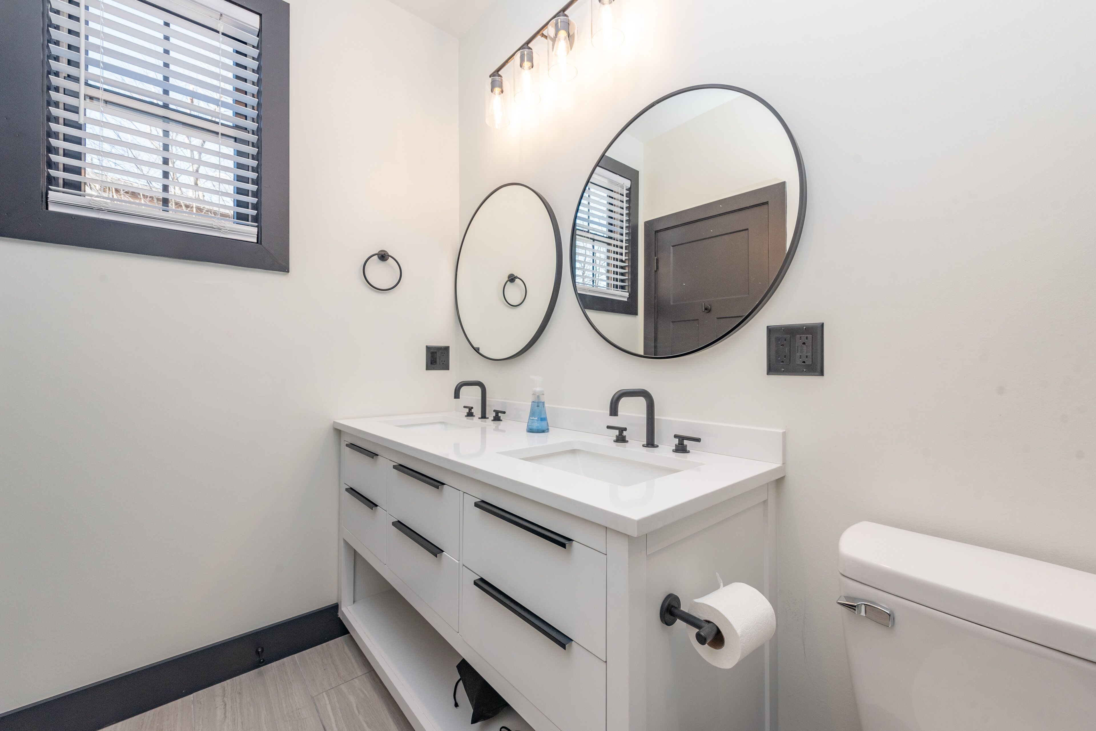 A modern bathroom with a white vanity, two sinks, a toilet, and three wall-mounted mirrors.