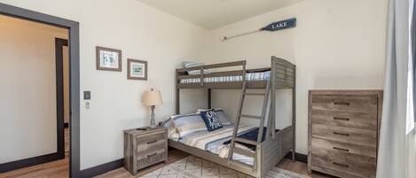 A bedroom with a bunk bed, a desk with a lamp, a dresser, a ceiling fan, and a sign on the wall.