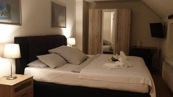 Ein ordentlich bezogenes Bett mit Kissen, ein Nachttisch mit Lampe, ein Spiegel und ein an der Wand befestigter Fernseher.