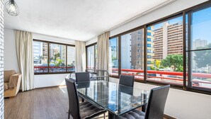 Een moderne hotelkamer met een glazen eettafel, comfortabele zitplaatsen, grote ramen met uitzicht op de stad en een accentmuur van baksteen.