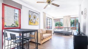Een ruime woonkamer met een bank, een eettafel met stoelen, een plafondventilator en een groot raam met gordijnen.