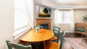 A dining area with a wooden table, green chairs, a fireplace, and a painting on the wall.